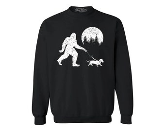 May include: Black sweatshirt featuring a white graphic of Bigfoot walking a dachshund under a full moon. The graphic has a distressed look.