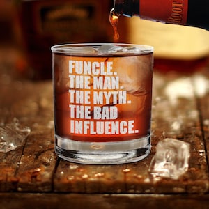 May include: A clear glass with a brown liquid and ice inside. The glass has the text "FUNCLE. THE MAN. THE MYTH. THE BAD INFLUENCE." printed on it.
