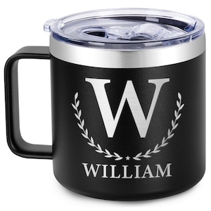 以下が含まれることがあります： 銀色の蓋と銀色の「W」のモノグラムが施された黒いステンレス製のトラベルマグ。周りに花輪があり、その下に「WILLIAM」という名前が書かれています。