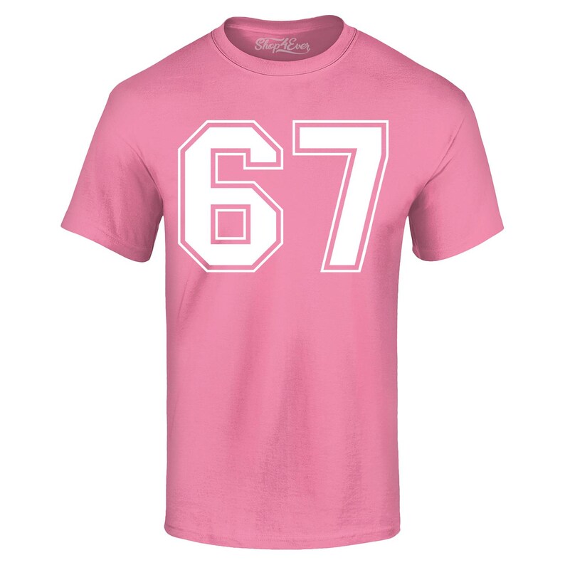 May include: A pink t-shirt with the number "67" in white block letters. The number is outlined in white and centered on the front of the shirt. The shirt has short sleeves and a crew neck.