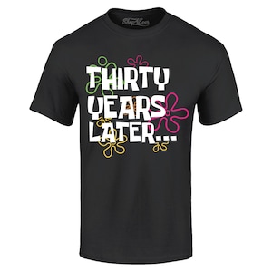 May include: Black t-shirt with the text "THIRTY YEARS LATER..." in white, with colorful flower-like designs. The shirt has a crew neck and short sleeves. The Shop4Ever logo is visible at the top.