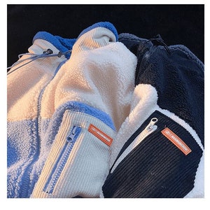 May include: Two fleece jackets with contrasting panels of blue, white, and black. Both jackets have a zipper closure and a small orange label with the text "MAXIMUNGIRL" on the sleeve.