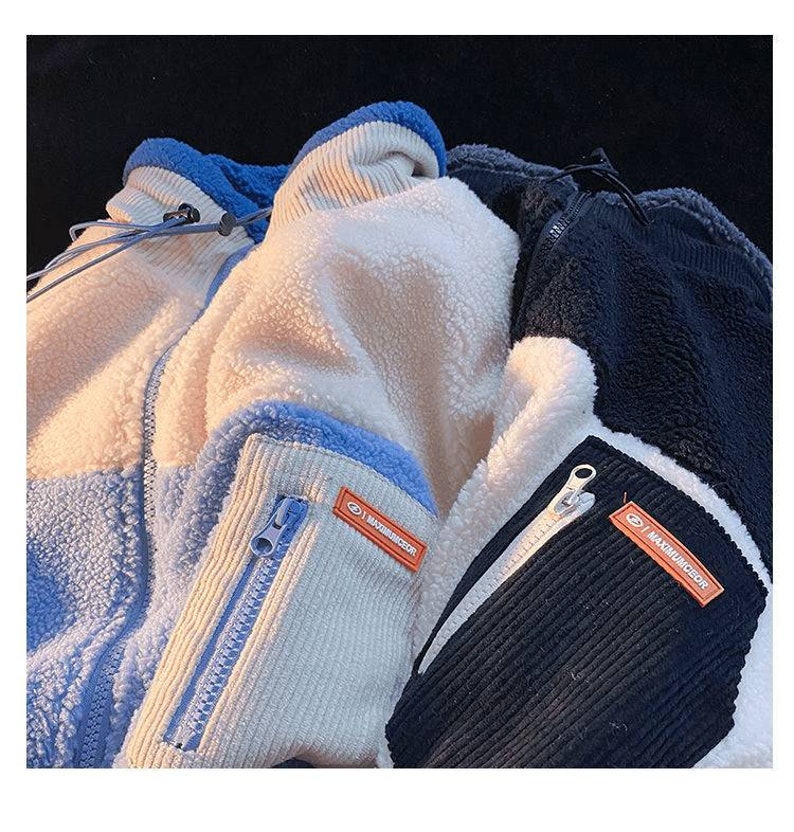 May include: Two fleece jackets with contrasting panels of blue, white, and black. Both jackets have a zipper closure and a small orange label with the text "MAXIMUNGIRL" on the sleeve.