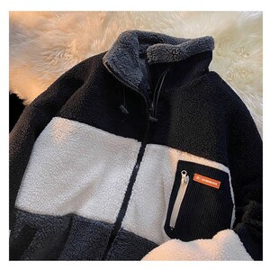 May include: A black, white, and gray fleece jacket with a zipper closure and a patch pocket on the right side. The pocket has a zipper and a small orange label with the text "WATERPROOF" on it.