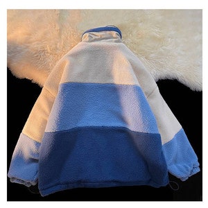 May include: A white, light blue, and dark blue fleece jacket with a high collar and zipper closure.