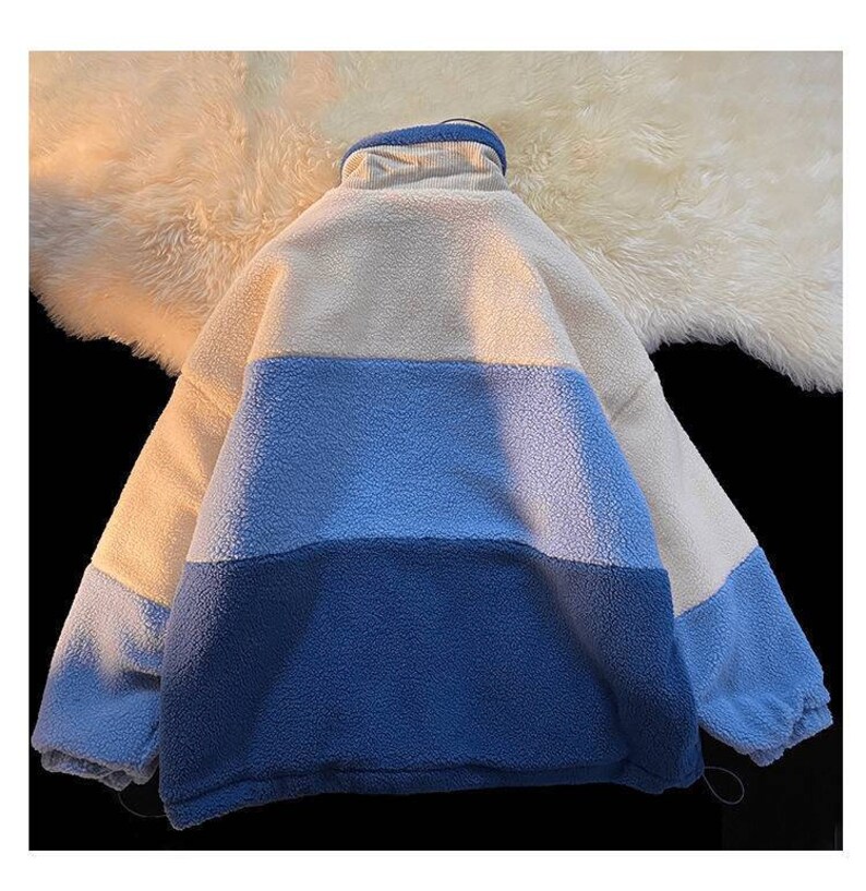 May include: A white, light blue, and dark blue fleece jacket with a high collar and zipper closure.