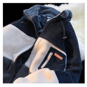 May include: A black, white, and gray fleece jacket with a zipper closure and a small pocket on the left sleeve. The pocket has a zipper and a small orange label with the text "MASSDIRECTION" on it.