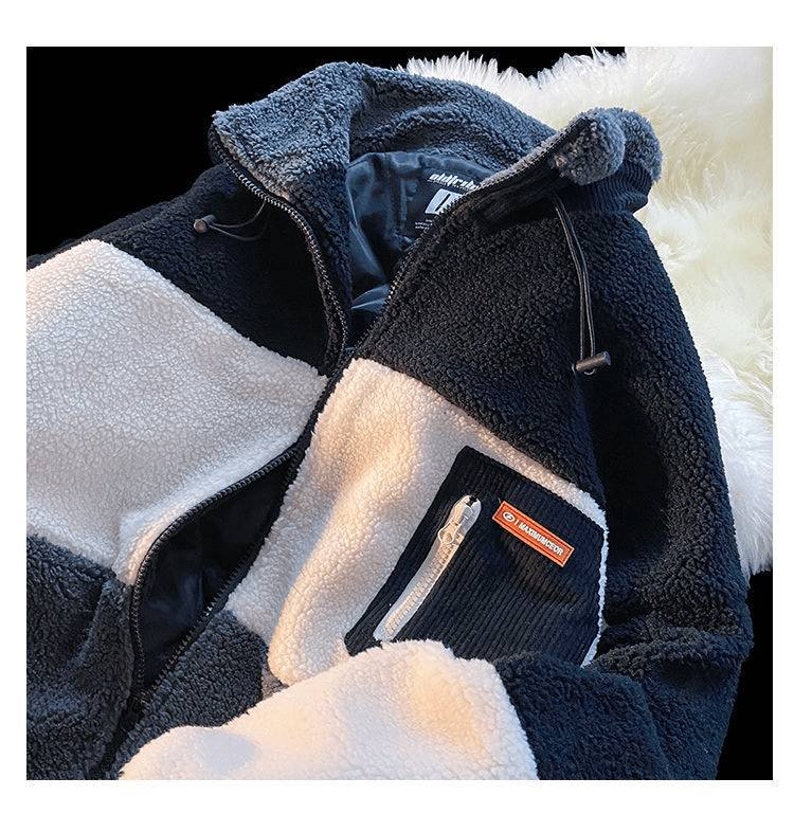 May include: A black, white, and gray fleece jacket with a zipper closure and a small pocket on the left sleeve. The pocket has a zipper and a small orange label with the text "MASSDIRECTION" on it.