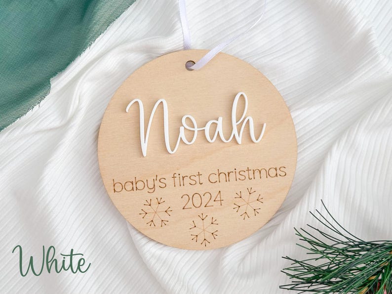 May include: White wooden ornament with the name "Noah" and the text "baby's first christmas 2024" with snowflake designs.