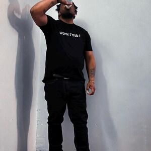 May include: A black short-sleeved t-shirt featuring the white text "I don't know" printed across the chest. The shirt is paired with black pants and black sneakers, creating a monochromatic look. The garment is worn by an individual drinking water.