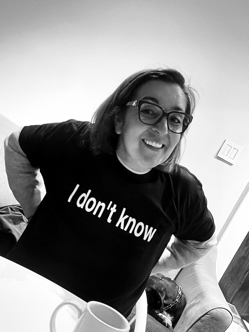 May include: A black short-sleeved t-shirt featuring the white text "I don't know" printed across the chest. The shirt has a crew neckline and is worn by an individual with dark hair and glasses, visible from the chest up in this black and white image.