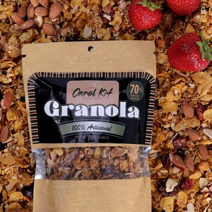 Puede incluir: Una bolsa de papel marr&oacute;n con una ventana de pl&aacute;stico transparente que muestra granola en su interior. La bolsa tiene una etiqueta negra con el texto "Carol Kit HEALTHY Granola 70% Whole Grains 100% Artesanal NET WT 6 OZ (168Gr)".