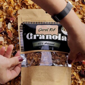 Puede incluir: Una bolsa de papel marr&oacute;n con una ventana de pl&aacute;stico transparente que muestra granola en su interior. La bolsa tiene una etiqueta negra con el texto "Carol Kit Healthy Granola 100% Artesanal NET WT 6 OZ (168G)".