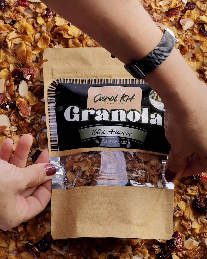 Puede incluir: Una bolsa de papel marr&oacute;n con una ventana de pl&aacute;stico transparente que muestra granola en su interior. La bolsa tiene una etiqueta negra con el texto "Carol Kit Healthy Granola 100% Artesanal NET WT 6 OZ (168G)".