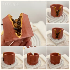 May include: Several small, geometric, terracotta-coloured planters. Each planter has a gold-painted accent and is filled with tiger eye stones. The text "Tiger eye" is visible in the image.