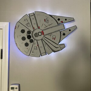 Könnte beinhalten: Eine weiße Wand mit einer Schwarzweißzeichnung des Raumschiffs Millennium Falcon aus Star Wars. Die Zeichnung ist auf weißem Hintergrund und hat rote Akzente.