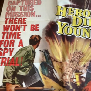 Op de afbeelding: Een vintage filmposter voor de film "Hero Die Young" met een man in een groen shirt die een geweer vasthoudt. De poster heeft een geel en rood kleurenschema met de titel in grote gele letters. De tekst op de poster luidt: "Als hij tijdens deze missie wordt gevangen genomen... is er geen tijd voor een spionageproces!"