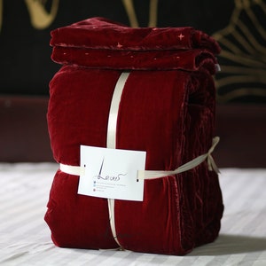 May include: A red velvet quilt folded and tied with a white ribbon. The quilt is labeled "Levis" on a white tag.