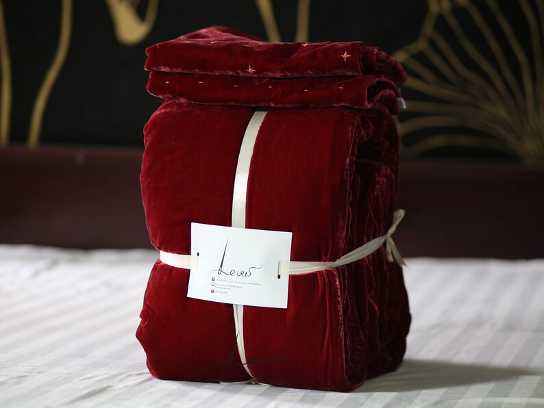 May include: A red velvet quilt folded and tied with a white ribbon. The quilt is labeled "Levis" on a white tag.