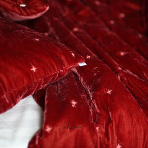 May include: Red velvet bedding with a subtle star pattern. The fabric is soft and luxurious, perfect for a cozy bedroom.