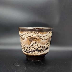 May include: A ceramic cup with a textured, wave-like pattern in shades of brown, beige, and white. The cup has a dark brown base and rim, and the design gives it a unique, handcrafted appearance. The cup is likely for drinking.