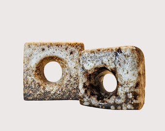 May include: Two ceramic square beads with a central circular hole. The beads have a speckled, off-white and brown glaze, giving them a rustic appearance. The design is simple and modern.
