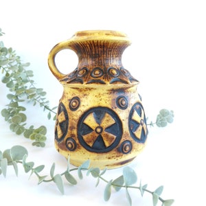 May include: A yellow ceramic pitcher with a brown and black geometric design. The pitcher has a wide mouth and a handle.