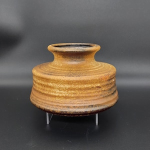 Peut inclure: Un vase en céramique brun avec une base large et un col étroit. Le vase a une surface texturée et un glaçage brun foncé.