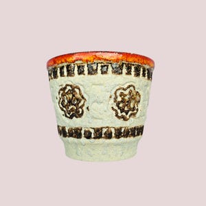 Pode incluir: Pequeno vaso de cerâmica texturizada com base creme. Apresenta desenhos florais castanhos e uma faixa de retângulos castanhos. A borda é laranja vibrante. Adequado para plantas pequenas ou como um adorno doméstico único.