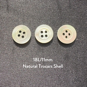 May include: Three round, off-white natural shell buttons with four holes each, arranged on a dark grey textured surface. The buttons are 11mm in diameter. Text below reads "18L/11mm Natural Trocars Shell."