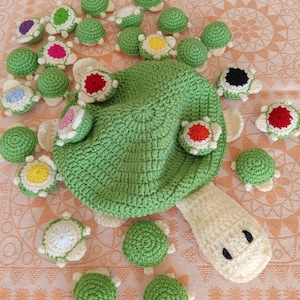 Op de afbeelding: Een verzameling gebreide groene schildpad speelgoed. De grotere schildpad heeft een wit hoofd en poten. De kleinere schildpadden hebben kleurrijke accenten op hun schilden.