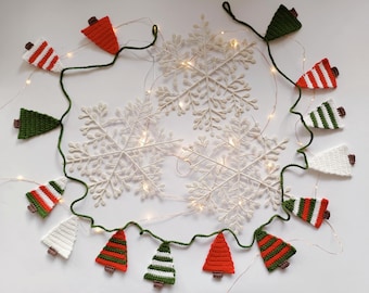 Könnte beinhalten: Eine festliche Weihnachts-Girlande mit gehäkelten Baumschmuck in Rot, Grün und Weiß, auf einer grünen Schnur aufgereiht. Die Girlande ist um weiße Schneeflocken-Dekorationen und funkelnde Lichterketten angeordnet und schafft eine gemütliche Urlaubsszene.