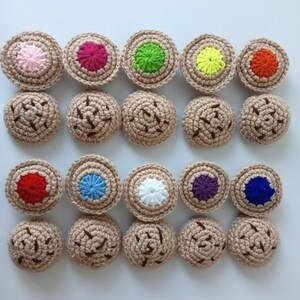 May include: Twenty crocheted cookies with various colored centers. The cookies are beige with brown stitching and are arranged in three rows.