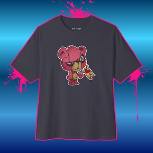 Peut inclure: Un t-shirt gris foncé avec un motif d'ours en peluche rose à l'expression colérique et à la bouche cousue. L'ours tient un petit drapeau en lambeaux orné d'un cœur rouge. Le texte "Daf Vadgr" est imprimé en blanc sur l'étiquette du col.