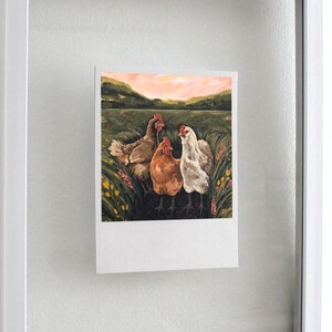 May include: A rectangular print featuring a painting of three chickens standing in a grassy field with yellow and pink flowers. The chickens are brown, orange, and white. The background shows rolling green hills under a soft pink and orange sunset sky.