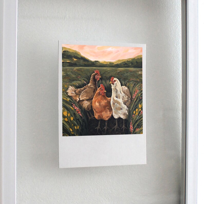 May include: A rectangular print featuring a painting of three chickens standing in a grassy field with yellow and pink flowers. The chickens are brown, orange, and white. The background shows rolling green hills under a soft pink and orange sunset sky.