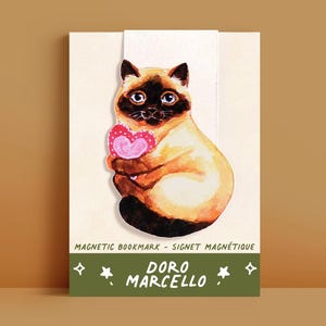 Peut inclure: Marque-page magnétique avec une illustration de chat siamois tenant un cœur rose. Le chat a des marques marron et noires et des yeux bleus. Le marque-page porte l'inscription "Doro Marcello" et "Magnetic Bookmark - Signet Magnétique" sur une bannière verte.
