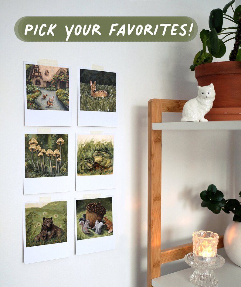 May include: Six square art prints with white borders are taped to a wall, featuring illustrations of a cottage, a deer, mushrooms, frogs, a bear, and squirrels with an acorn. The text PICK YOUR FAVORITES! is displayed in white on a green background.