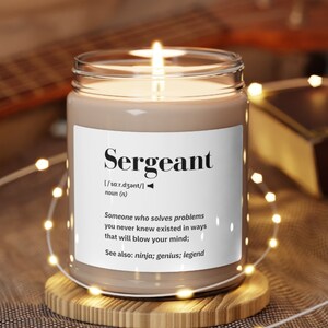 May include: A lit candle in a clear glass jar with a white label that reads "Sergeant." The label includes a definition and the phrases "Someone who solves problems" and "See also: ninja; genius; legend." The candle sits on a wooden coaster.