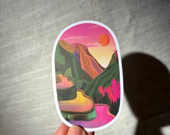 May include: Oval sticker depicting a colourful landscape with a pink sky and orange sun. The design includes green mountains, a pink river, and terraced fields. The sticker has a white border.