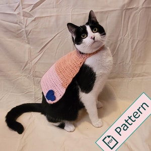 May include: A black and white cat wearing a pink and peach crocheted cat cape with a blue heart. The cape is a crochet pattern for a cat costume. The text "Pattern PDF" is on a pink rectangle.