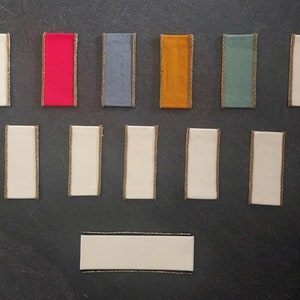 May include: Assortment of twelve fabric ribbon samples with gold trim. The ribbons are in various colors, including red, blue, green, orange, and white.