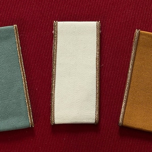 Könnte beinhalten: Drei Stoffmuster mit goldener Einfassung. Die Muster sind türkis, weiß und orange.