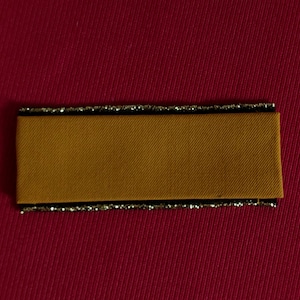May include: A brown fabric label with a black border and gold glitter trim. The label is on a red background.