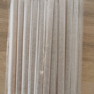May include: A package of white paper straws, wrapped in clear plastic. The straws are bundled together and are ready to be used.