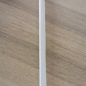 May include: A white paper drinking straw, wrapped in a white paper wrapper, is lying flat on a wooden surface.
