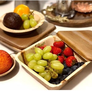 May include: A set of four palm leaf bowls, two with lids, filled with fresh fruit and berries. The bowls are perfect for serving snacks or meals.