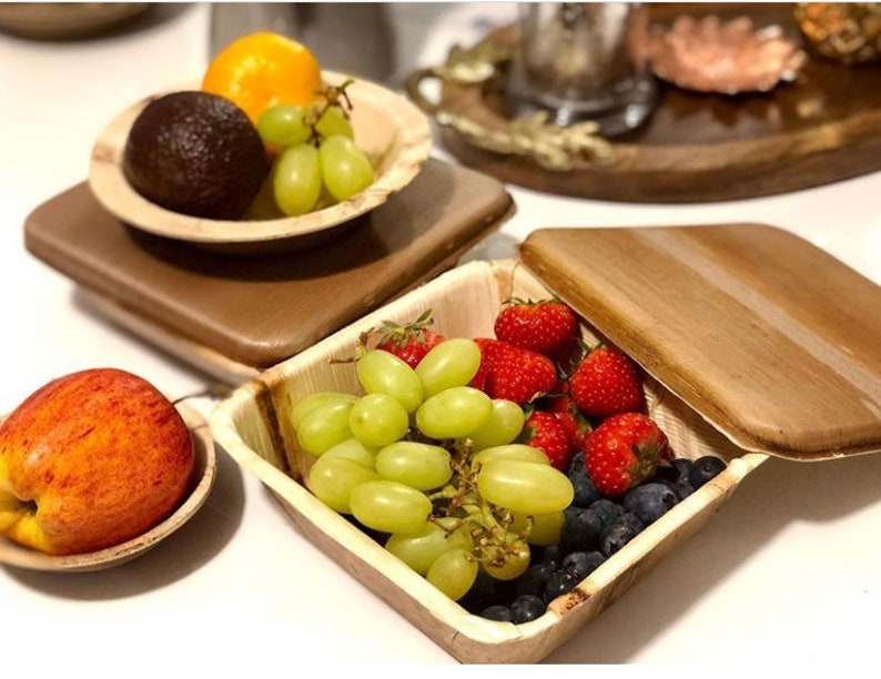 May include: A set of four palm leaf bowls, two with lids, filled with fresh fruit and berries. The bowls are perfect for serving snacks or meals.