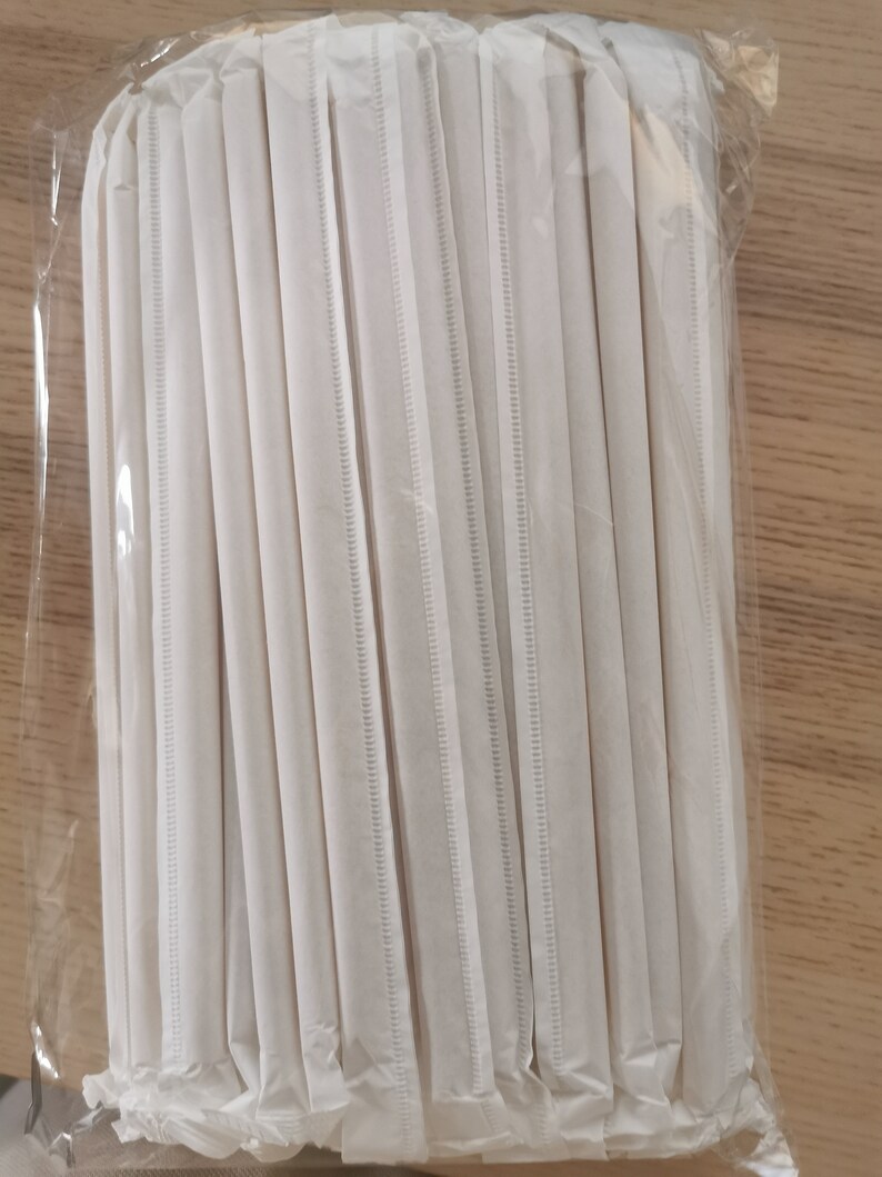 May include: A bundle of white paper straws wrapped in clear plastic. The straws are bundled together and ready to be used.