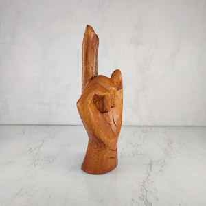 May include: A wooden hand sculpture with the index finger pointing up, carved in a light brown color.